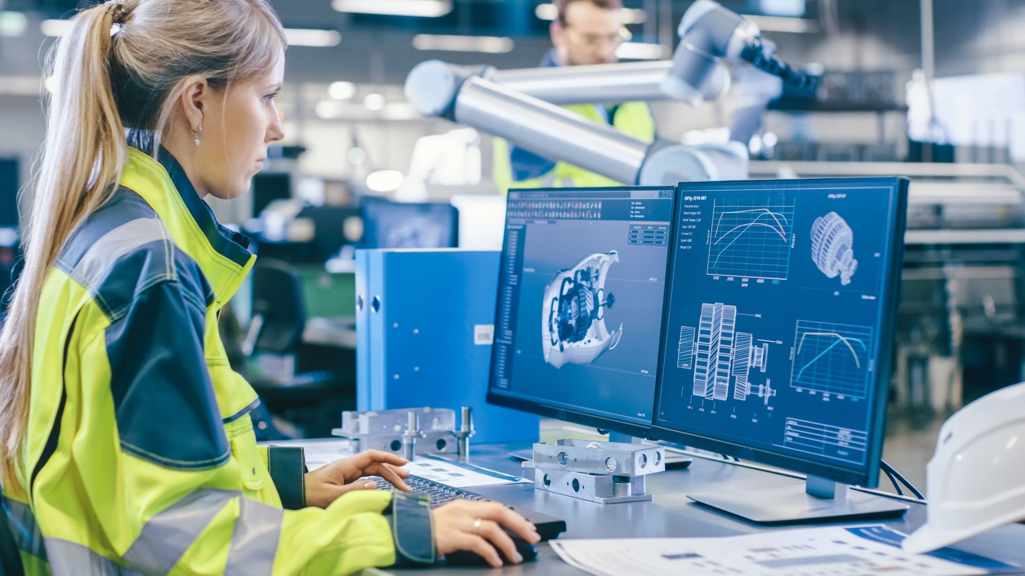 Engineer in werkkleding werkt aan een 3D-ontwerp op twee schermen in een moderne productiehal